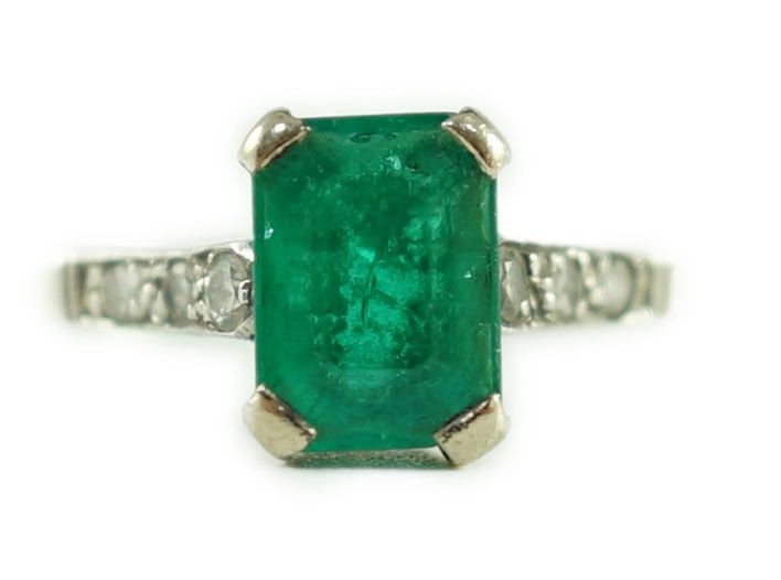 A white gold and single stone emerald ring, with six stone diamond set shoulders